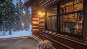 Eine Blockhütte mit Whirlpool, ein Fenster mit Blick auf den verschneiten Wald und ein Schild, das einen Kamin anzeigt.