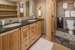 Une salle de bain avec des meubles en bois, deux lavabos, des toilettes et un miroir.