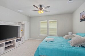 A bedroom with a bed, a TV, a ceiling fan, and a window with blinds.