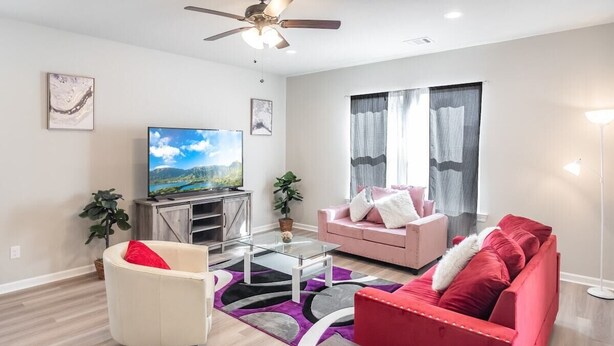 A modern living room with a flat-screen TV, a red sofa, a white armchair, and a coffee table. - Stay with Style and Cheer for the Tigers -  CB1029 (Baton Rouge)