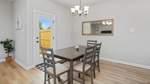 A dining area with a table and chairs, a chandelier, a door leading outside, and a mirror on the wall. - Stay with Style and Cheer for the Tigers -  CB1029 (Baton Rouge)