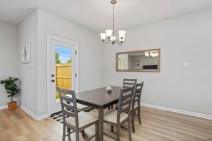 A dining area with a table and chairs, a chandelier, a door leading outside, and a mirror on the wall.