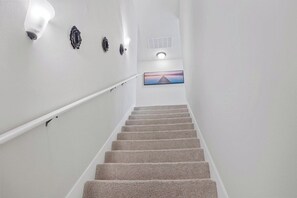 Uma escada com corrimão, luminária na parede e um quadro no topo.