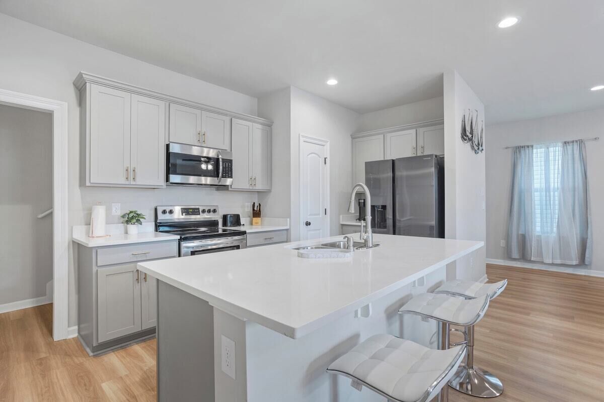 A modern kitchen with white cabinetry, stainless steel appliances, and a central island with bar stools.