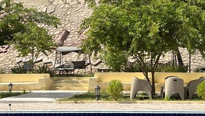 Una piscina con sillas de descanso y una pared de piedra con una torre al fondo.