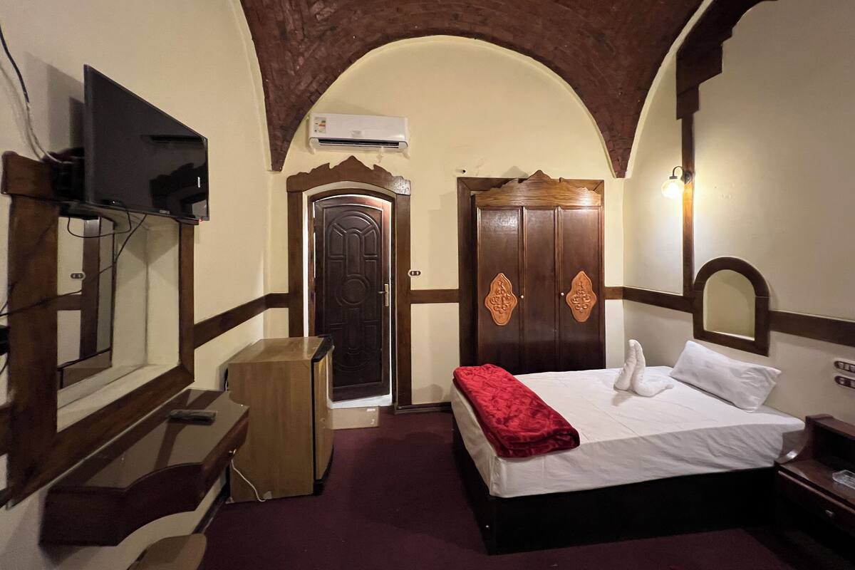 A hotel room with a bed, a TV, a wardrobe, and a mirror.