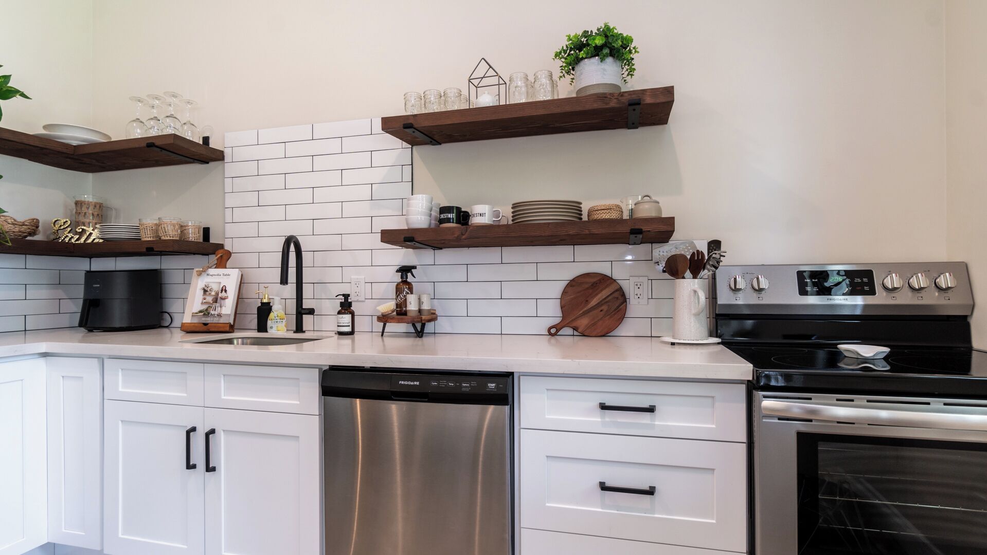 A modern kitchen with white cabinets, stainless steel appliances, and wooden shelves.