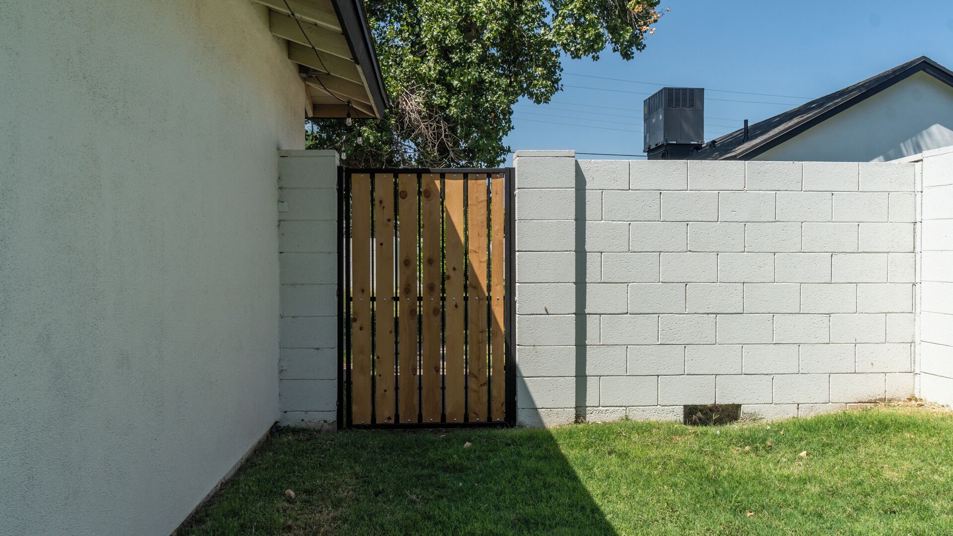 Un patio trasero amurallado con un muro de concreto, una puerta de madera y césped.