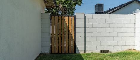 Un patio trasero amurallado con un muro de concreto, una puerta de madera y césped.