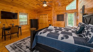 Une chambre dans une cabane en bois, comprenant un lit, un bureau, une chaise, un téléviseur et un ventilateur de plafond.
