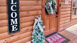 Une cabane en bois avec une pancarte « BIENVENUE », une porte décorée d’une guirlande et un petit sapin de Noël.