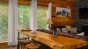 L’intérieur chaleureux d’un chalet avec une longue table en bois, un canapé en cuir et une cheminée en pierre.