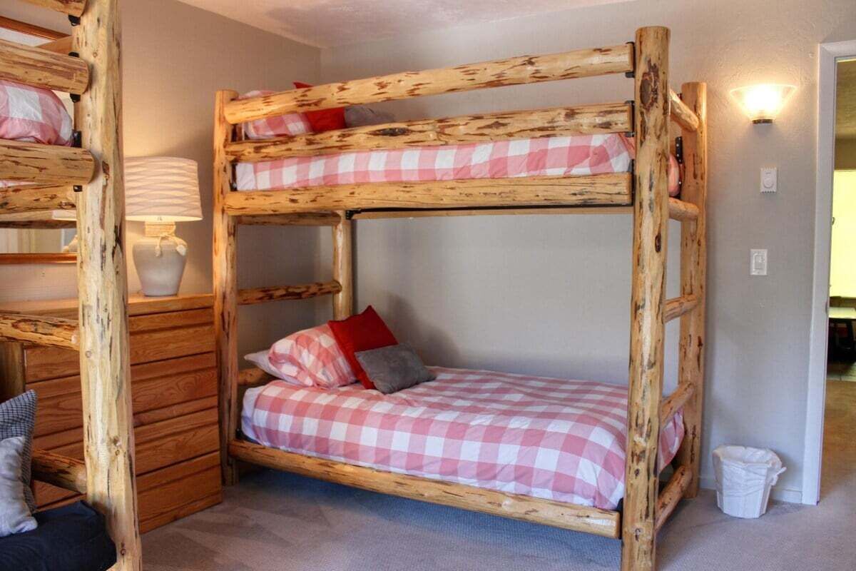 Un lit superposé avec une couvre-lit à carreaux et des oreillers, une lampe de chevet et une table de chevet en bois.