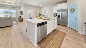 Een moderne keuken met een centraal eiland, witte kasten, een roestvrijstalen koelkast en een blauwe deur.