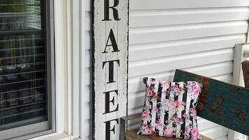 A wooden sign with the word "GRATEFUL" mounted on a white wall next to a bench with a floral pillow.