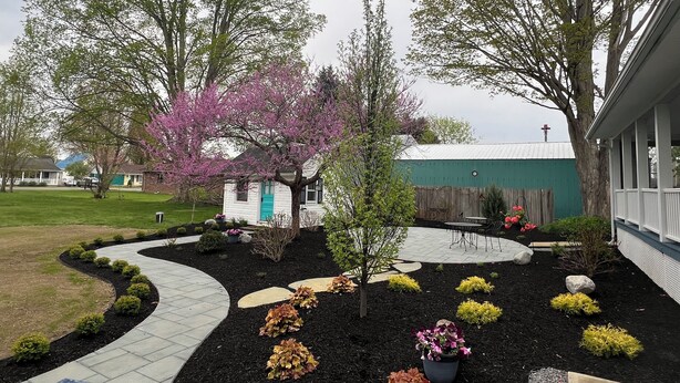 A landscaped garden with a pathway leading to a building with a green roof. - Quaint historic home in the heart of Bemus Point Village- a stroll to the water! (Bemus Point)