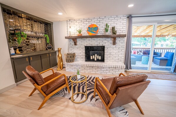 Ein modernes Wohnzimmer mit Kamin, Ledersesseln, einem Zebra-Teppich und einer Bar mit Pflanzen und Gläsern.