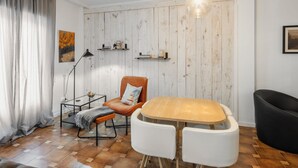 A modern living room with a wooden dining table, two white chairs, a leather armchair, a black sofa, and a wooden wall with shelves.