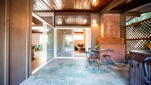 Un patio al aire libre con un muro de ladrillo, techo de madera y una zona de estar con mesa y sillas.