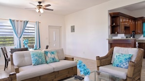 A living room with a sofa, two armchairs, a glass coffee table, and a ceiling fan.