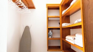 A small, neatly organized closet with wooden shelves, a hanging rack, and an ironing board.