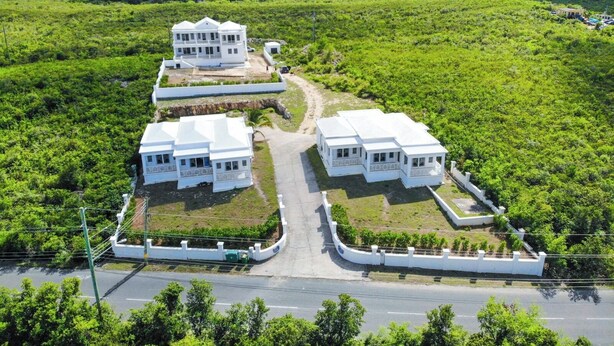 A large white building with multiple sections, surrounded by lush greenery and a clear sky.