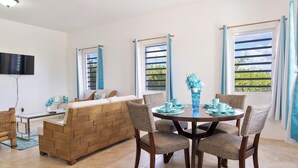 A modern living room with a wooden sofa, a dining table with chairs, and a TV mounted on the wall.