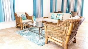 A living room with wicker furniture, a glass coffee table, and blue and white curtains.