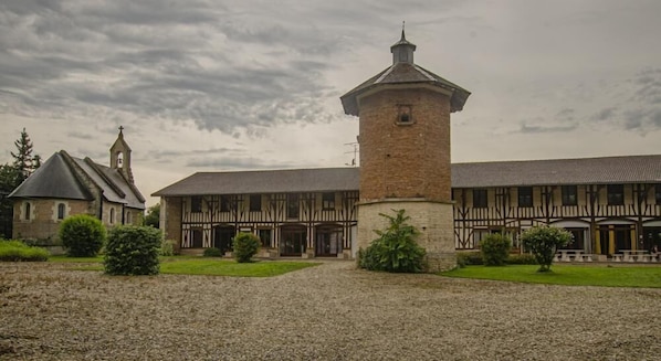 Un edificio histórico con una torre destacada, una iglesia y un amplio patio con caminos de grava y áreas verdes.