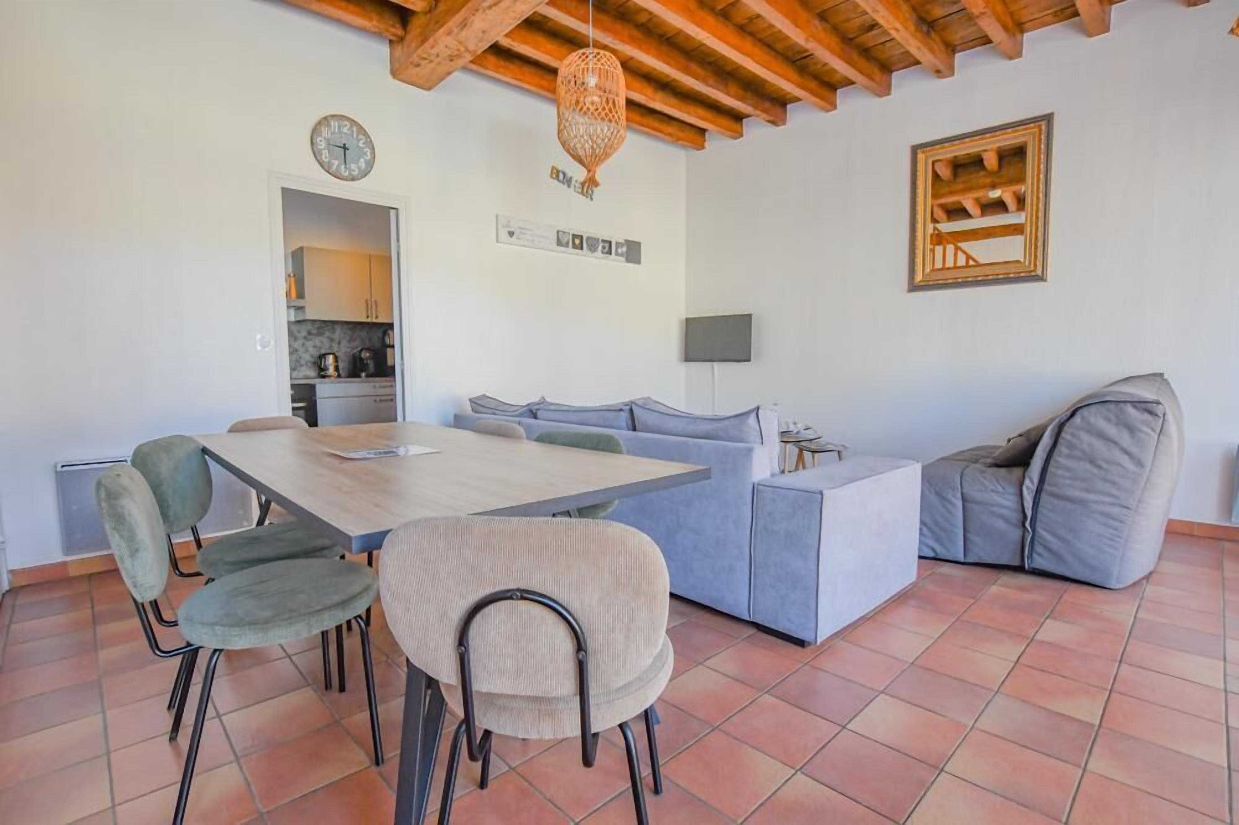 Una sala de estar moderna con una mesa de comedor, un sofá y sillas. Se ve una cocina al fondo.