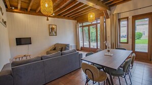 Una sala de estar con un sofá gris, vigas de madera en el techo, un televisor y una mesa de comedor con sillas.