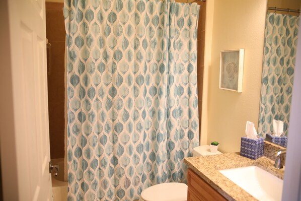 A bathroom with a patterned shower curtain, a toilet, a sink with a countertop, and a small framed picture on the wall. - The BEST View at Cinnamon Beach- Largest Ocean Unit, Sunrise and Sunset! (Palm Coast)