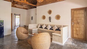 A spacious room with a high ceiling, a woven ceiling fan, a wooden door, and a sofa with cushions.