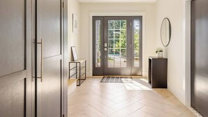 Ein moderner Flur mit einer dunklen Tür, einem kleinen Tisch mit einer Vase und einem Spiegel an der Wand.