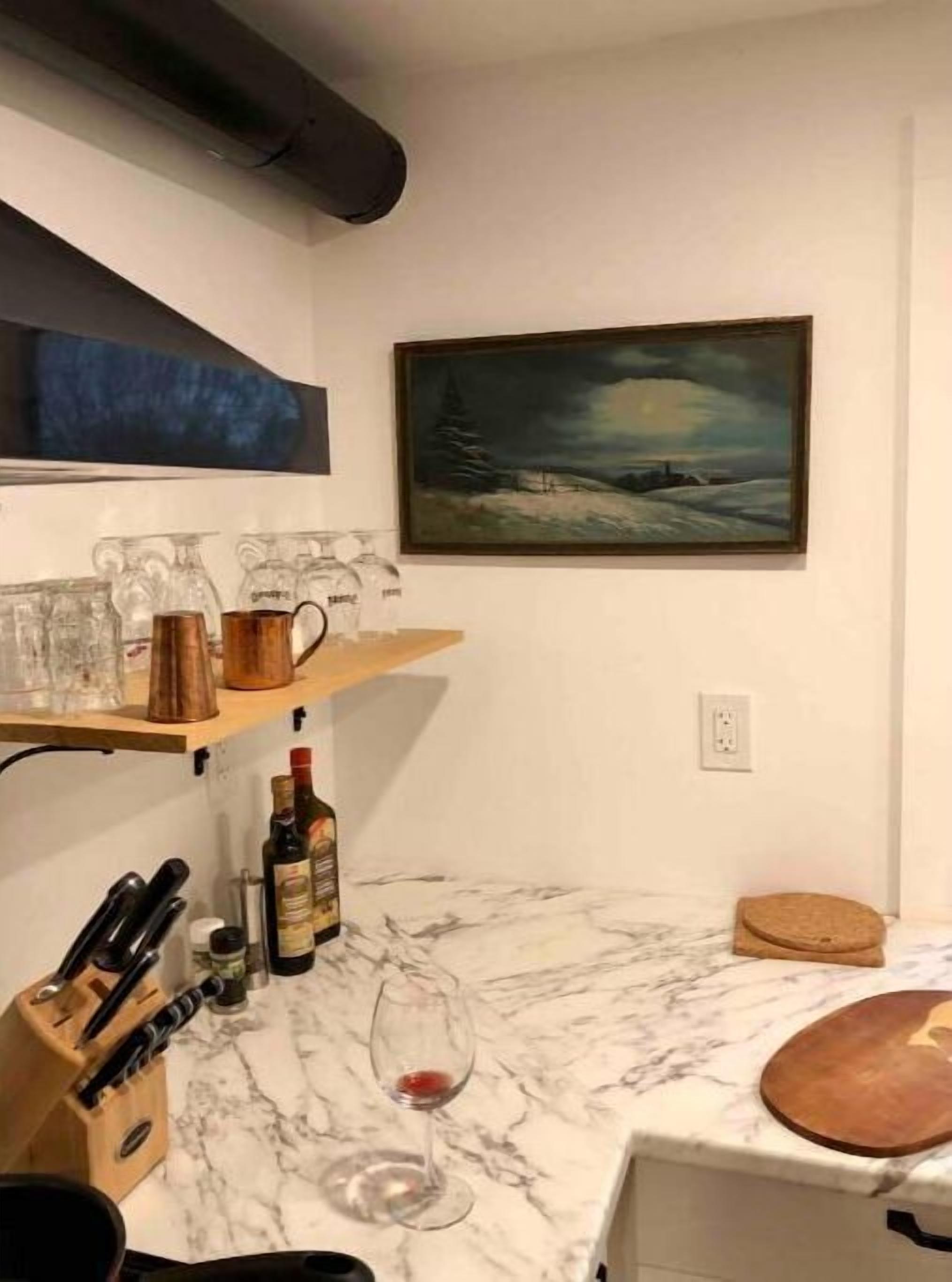 Eine Küche mit Marmorarbeitsplatten, Weingläsern und Flaschen. An der Wand hängt ein Gemälde und ein Regal mit Gläsern.