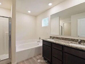 Enjoy a refreshing shower or soak in the standalone bathtub in this bathroom, featuring a large vanity and mirror.