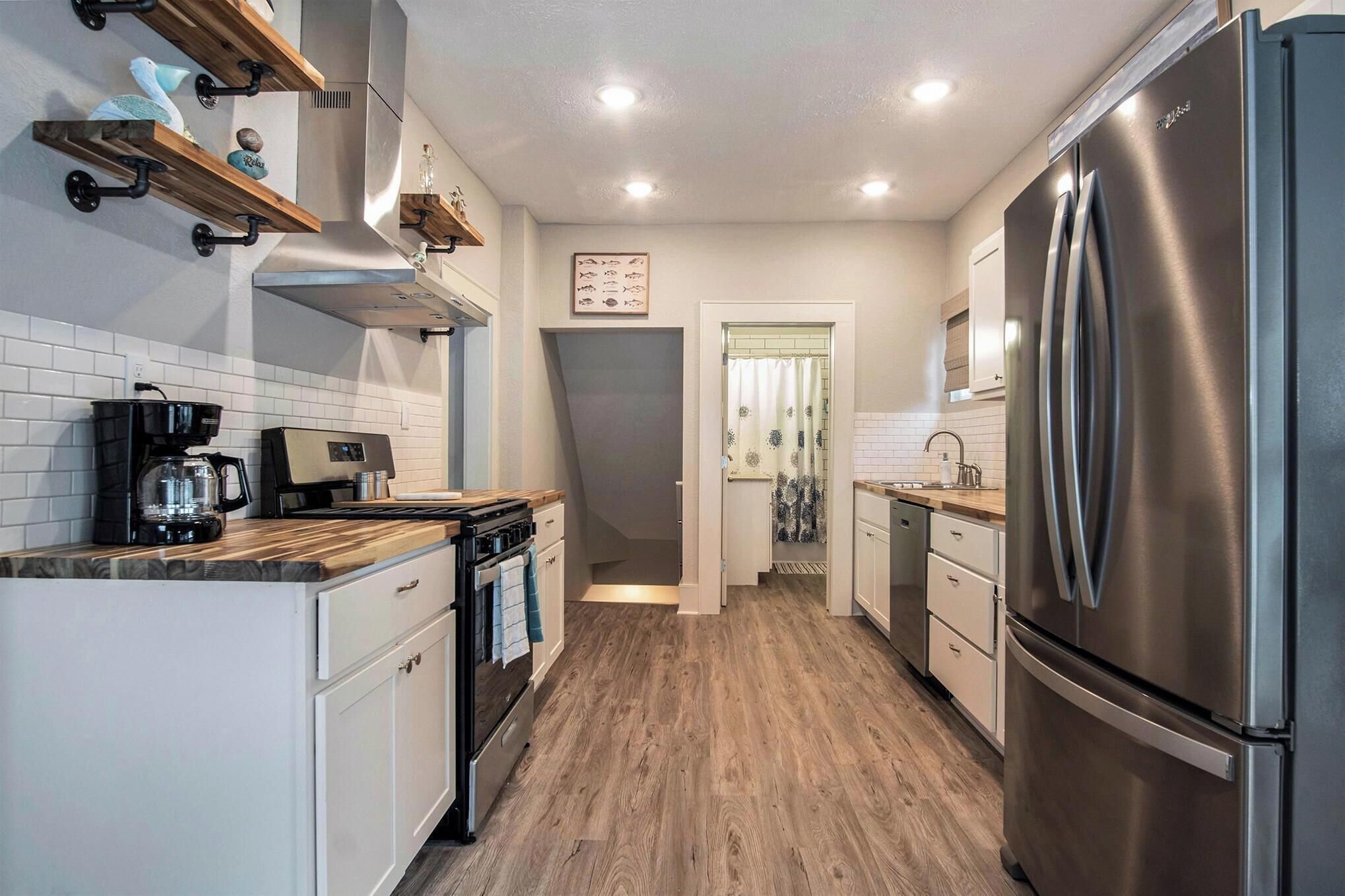 A modern kitchen with white cabinets, a stainless steel refrigerator, wooden countertops, and a built-in oven.