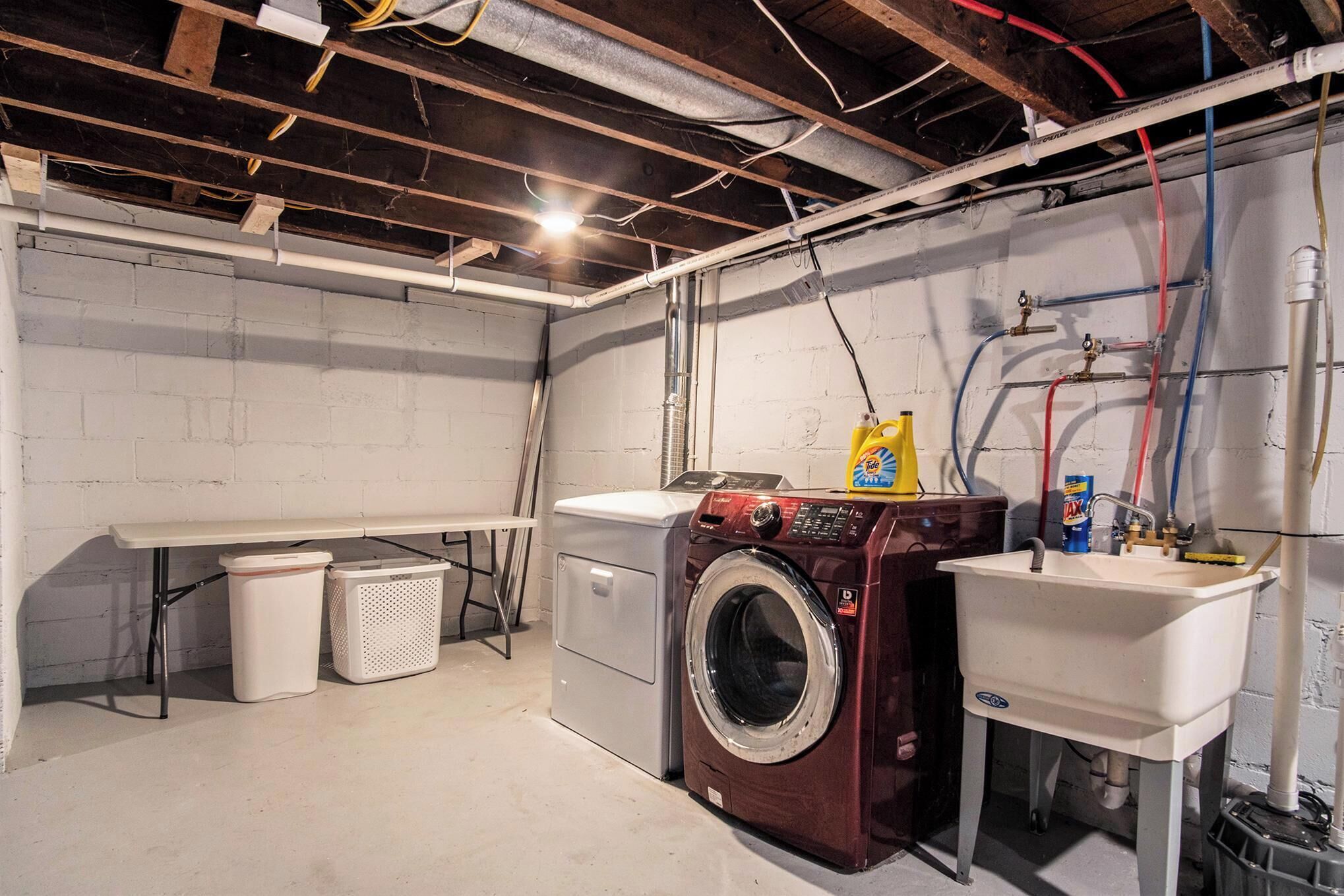 A laundry room with a washing machine, a sink, and a bench.