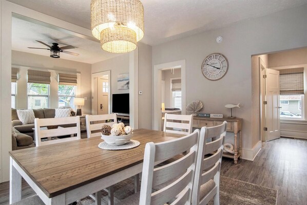 A dining area with a wooden table, white chairs, a chandelier, and a clock on the wall.