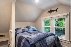 A bedroom with a bed, a window with a view of greenery, and a shark decoration on the wall.
