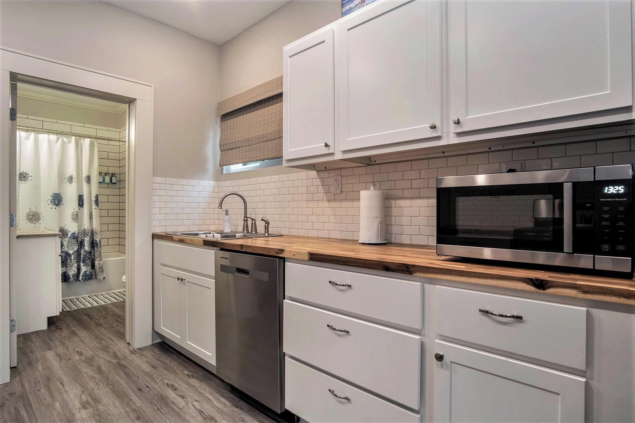A modern kitchen with white cabinets, a stainless steel dishwasher, a microwave, and a wooden countertop.