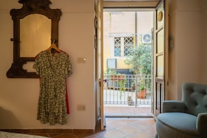 A room with a hanging dress, a chair, a mirror, and a view of a balcony with a gate.