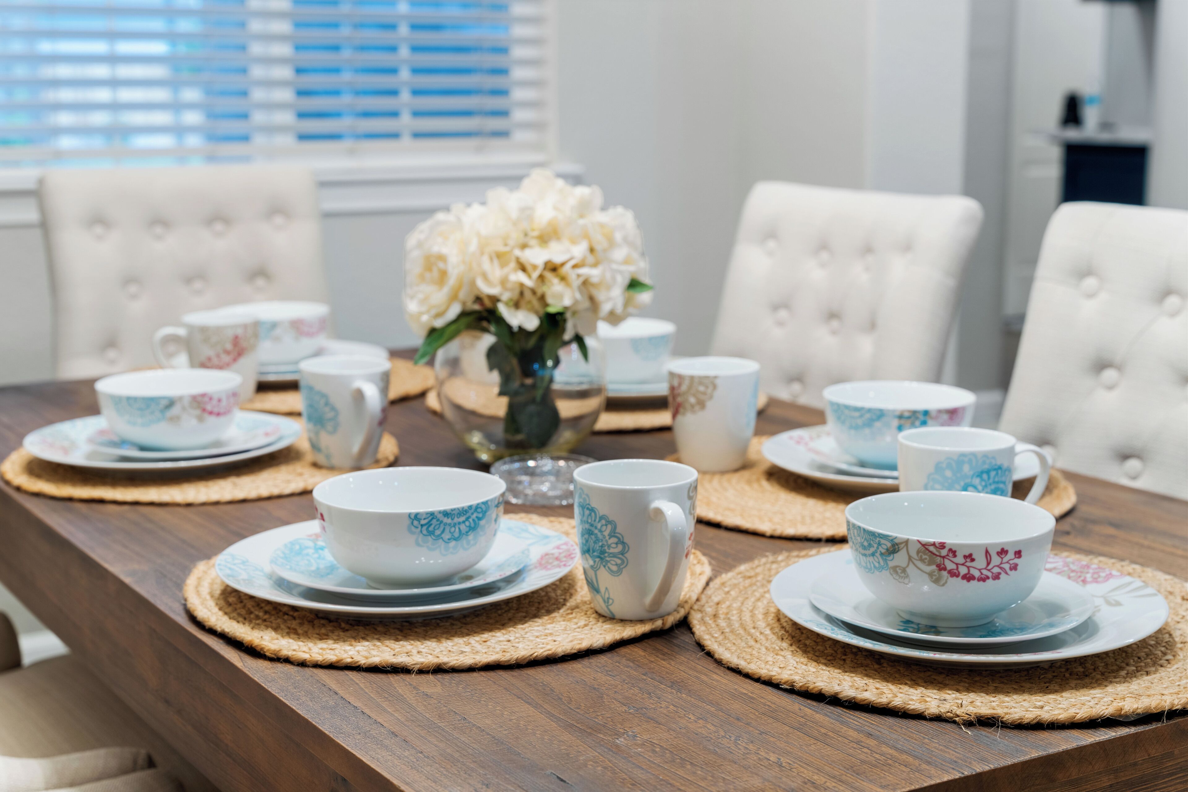 A dining table set with white and blue floral-patterned cups and saucers, placed on woven placemats.