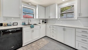 A modern kitchen with white cabinets, a dishwasher, and a window with blinds.