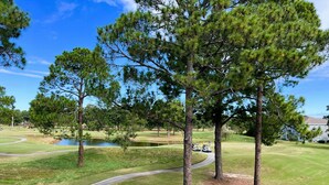 Un campo de golf con un estanque, árboles y un edificio al fondo.