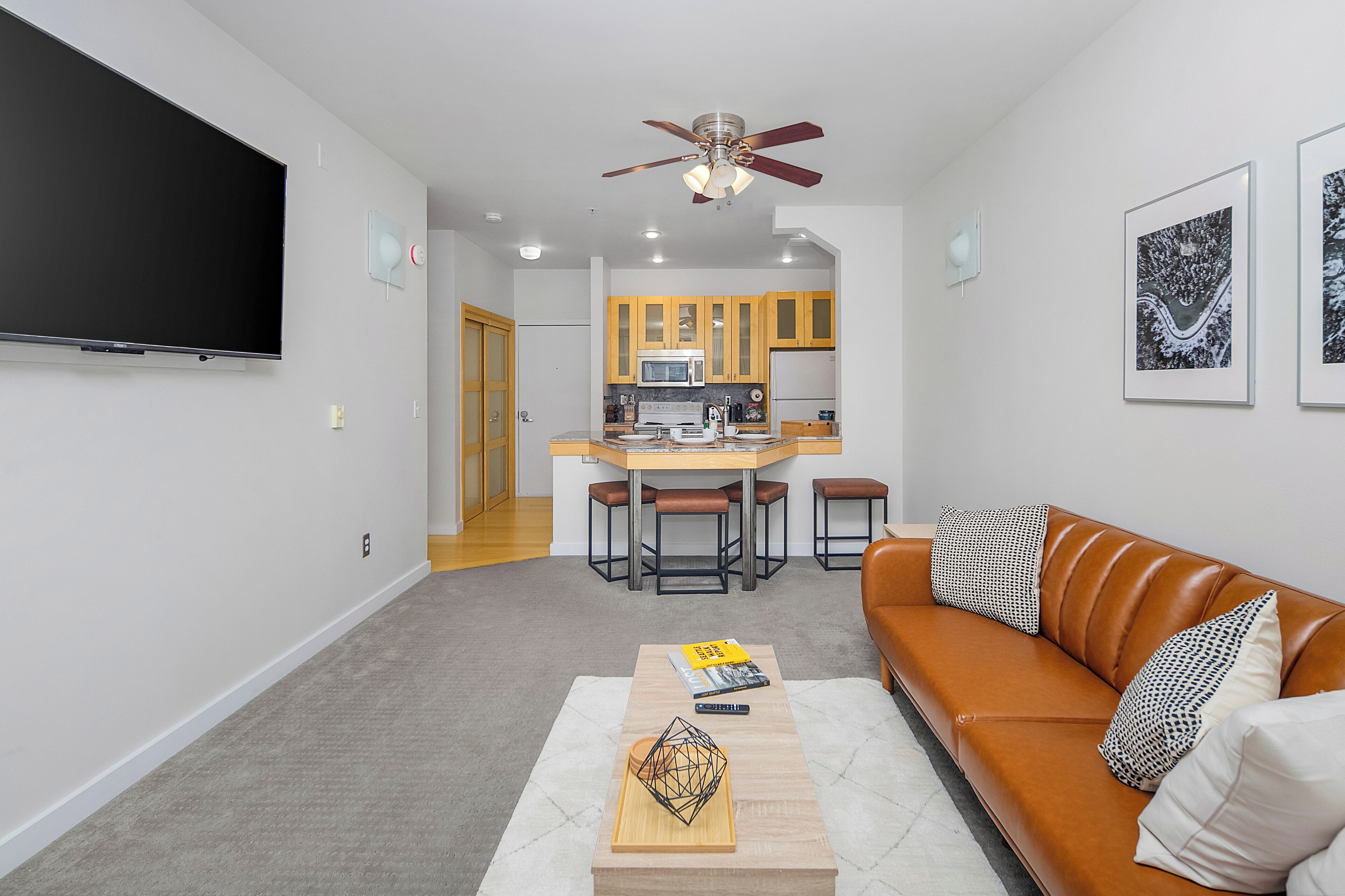 A modern living room with a flat-screen TV, a brown leather sofa, and a coffee table with books and a geometric sculpture.