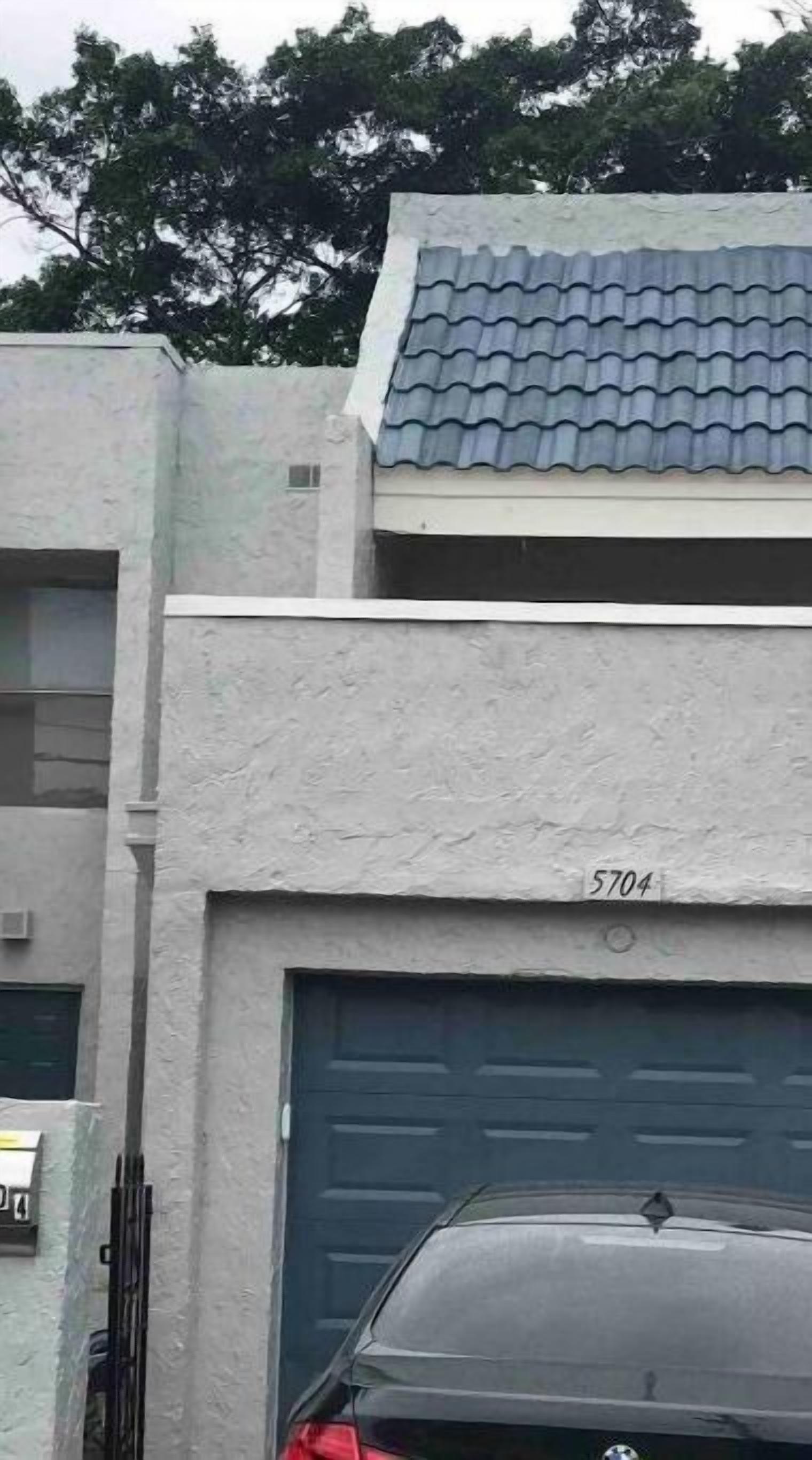 A building with a grey facade, a blue tiled roof, and a garage door marked with the number 5704.