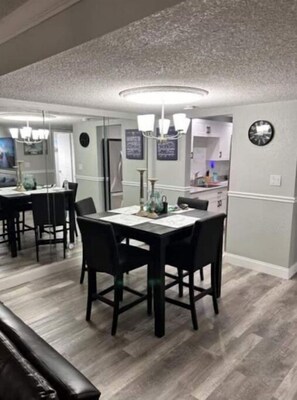 Un comedor con una mesa rectangular y cuatro sillas, un candelabro colgante y un reloj en la pared.