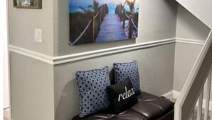 A staircase with a white railing, a brown leather bench with patterned cushions, and a framed picture of a sunset over a bridge. - On the beautiful lake, it is close to the airport, malls,restaurants ,beach etc. (Lauderhill)