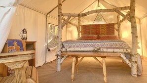 Una carpa rústica con un armazón de cama de madera, un farol y una manta estampada.